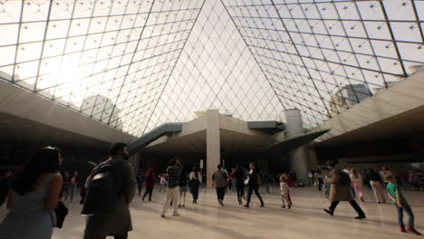 People-walking-under-the-famous-glass-pyramid-in-the-Louvre-Museum,-Paris,-France