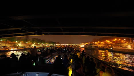 People-on-a-boat-on-the-Seine-river-in-Paris,-looking-at-the-cityscape,-at-night,-France
