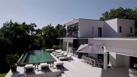 Woman-walks-out-of-glass-facade-,watches-over-calm-relaxing-pool-area,aerial