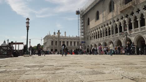 Turistas-Caminando-Por-El-Muelle-Junto-Al-Palacio-Ducal-Con-La-Biblioteca-Nazionale-Marciana-Al-Fondo-En-Venecia-En-Un-Día-Soleado