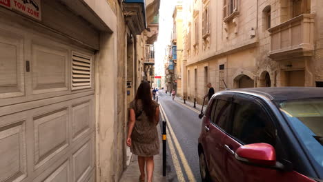 Folgen-Sie-Einer-Frau,-Die-Auf-Dem-Bürgersteig-Entlang-Einer-Schmalen-Straße-In-Der-Historischen-Altstadt-Von-Malta-Geht