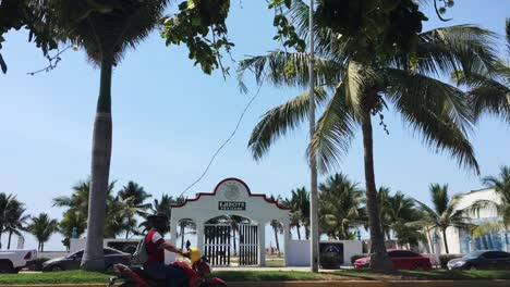 Road-with-car-traffic-passing-by-beach-entrance-in-tropical-Manzanillo,-Mexico