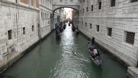 Iconic-view-of-the-waterway-from-the-Bridge-of-Sighs,-below-gondola-boats-pass-beneath-the-Ponte-Della-Paglia-bridge,-Venice,-Italy