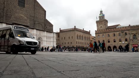 Tourists-Walking-Past-On-Piazza-Maggiore-With-Basilica-of-San-Petronio-And-Palazzo-Comunale-In-Background-In-Bologna