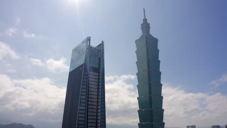 Aerial-backwards-shot-of-101-Tower-and-nan-shan-plaza-tower-in-Taipei-City-against-blue-sky-during-sunny-day-in-Taiwan
