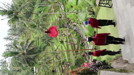 Behind-the-scenes-of-a-girl-in-a-long-red-train-dress-getting-a-photo-shoot-riding-a-swing-with-a-view-to-palm-tree-forest-and-rice-field-terraces-in-Alas-Harum,-Ubud-Bali