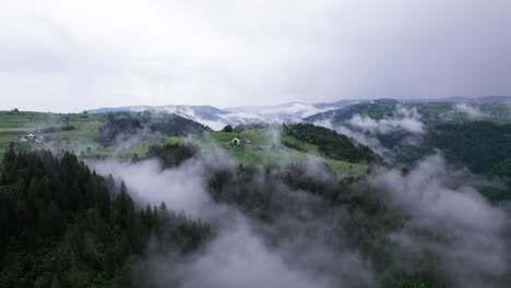 Aerial-view-of-a-village-on-forest-mountain-top-covered-by-fog,-Transylvania,-Romania