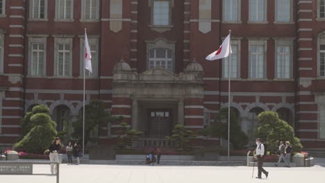 Front-view-of-the-classic-Tokyo-station-building-with-Japanese-flags-waving-on-the-sides-on-a-sunny-day-and-people-walking-around