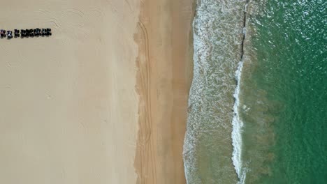 Green-ocean-water-crashes-on-golden-sandy-beach,-top-down-aerial-rising