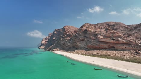 Boats-At-The-Azure-Watershore-Of-Shoab-Beach-Nearby-Rocky-Cliffs-During-Sunny-Day-In-Socotra-Island,-Yemen