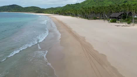 Aerial-dolly-above-gentle-crashing-waves-on-sloping-sand-shore-of-nacpan-beach