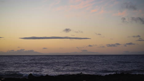 Sonnenuntergang-Mit-Kontrastierenden-Wolken-Am-Horizont-über-Wellen,-Die-Auf-Vulkangestein-Schlagen