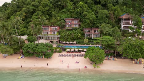 Rising-drone-reveals-tourists-enjoying-day-at-beach-and-luxury-cliffside-villas,-el-nido