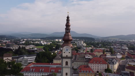 Aerial-circling-Klagenfurt-Cathedral-clock-tower,-revealing-cityscape,-Austria