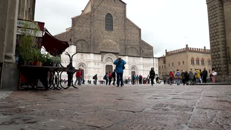 Autobús-Rojo-Pasando-Por-Piazza-Re-Enzo,-Cerca-De-Piazza-Maggiore,-Con-La-Basílica-De-San-Petronio-Al-Fondo