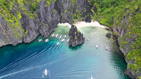 Bangka-paraw-canoes-enter-calm-deep-blue-water-bay-and-rocky-cliffs