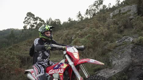 Plano-Medio-De-Un-Piloto-De-Motocross-Que-Intenta-Escalar-En-El-Suelo-En-Un-Hermoso-Paisaje-Montañoso