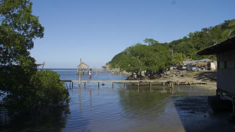 Playa-Punta-Gorda-En-Roatán,-Honduras-Durante-El-Día-Mientras-Una-Persona-Camina-Por-Un-Muelle-De-Madera-Hacia-La-Carretera