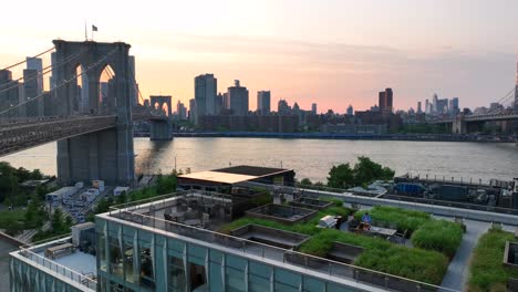 Vista-Aérea-De-Una-Pareja-Sentada-En-Un-Café-En-La-Azotea-Y-Disfrutando-De-La-Vista-Del-Horizonte-En-Nueva-York-Y-El-Puente-De-Brooklyn-Y-La-Hora-Del-Atardecer---Plano-Panorámico