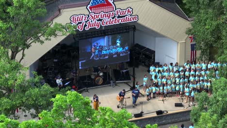 Drone-view-of-Lititz-Springs-Park-fourth-of-July-celebration-outdoor-performance-of-a-children's-church-choir-performing-for-the-community-members-on-a-beautiful-Sunday-afternoon