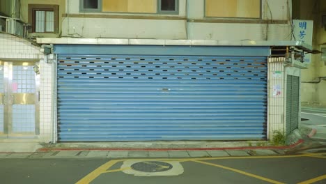 Blue-garage-grate-covering-shop-entrance-in-asia-at-night,-push-in