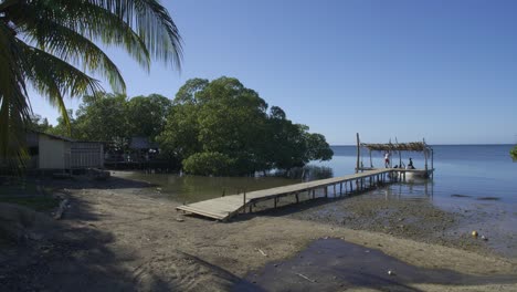 Der-Strand-Von-Punta-Gorda-In-Roatan,-Honduras,-Während-Der-Ebbe-Tagsüber,-Während-Die-Einheimischen-Ein-Kleines-Fischerboot-An-Einem-Holzsteg-Anlegen