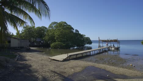 Punta-Gorda-beach-at-Roatan,-Honduras-during-the-daytime-low-tide-as-locals-dock-a-small-fishing-boat-to-a-wooden-pier