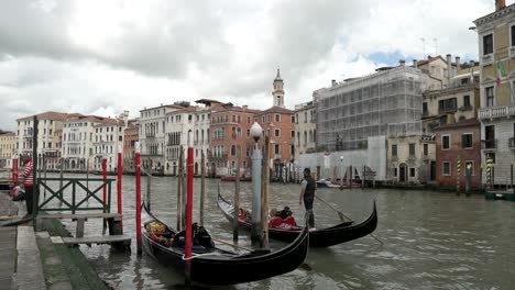 A-cinematic-view-of-a-boatman-is-riding-his-boat-on-the-water-Grand-Canal-in-Venice-with-colorful-buildings-and-clouds-are-at-the-background