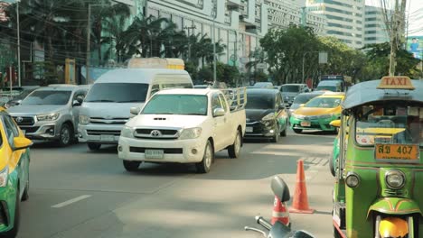 Vehicle-Traffic-Moving-Along-a-Main-Road-in-Bangkok-with-Green-Tuk-Tuk-Parked-in-Thailand
