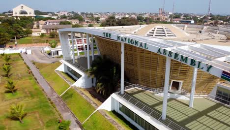 Ligera-Vista-Giratoria-Del-Moderno-Edificio-De-La-Asamblea-Nacional-De-Gambia-Con-El-Arco-22-Al-Fondo-En-Banjul