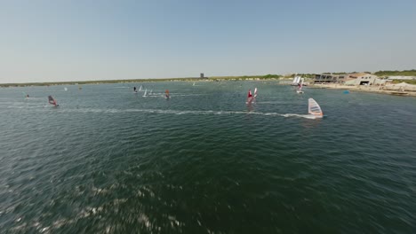 Low-to-high-drone-shot-showing-a-watersports-center-and-windsurfers-during-a-sunny-summer-day