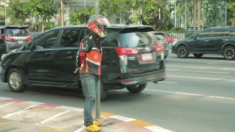 Conductor-De-Taxi-En-Moto-De-Pie-Contra-Un-Poste-En-La-Acera-De-Bangkok,-Tailandia