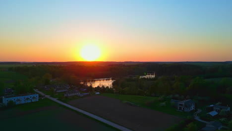 A-drone-pushes-over-farmland-with-the-sun-setting-over-water-on-the-horizon