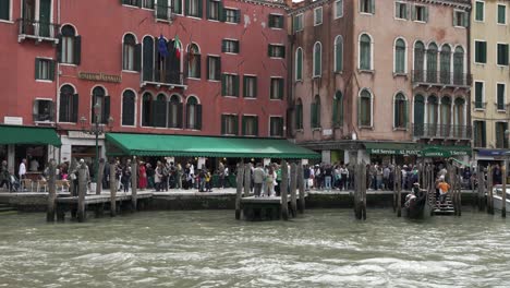 Vista-Del-Muelle-De-Góndolas-Al-Lado-De-La-Terminal-De-Ferry-De-Rialto-En-El-Gran-Canal-De-Venecia-Con-Multitudes-Ocupadas-Vistas-En-Segundo-Plano