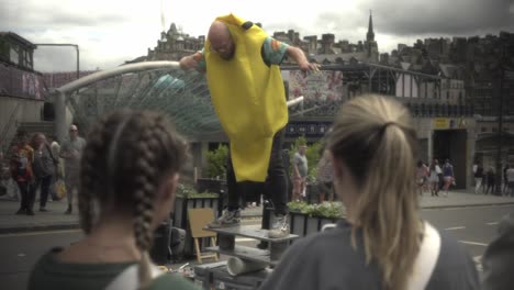 Witness-an-extraordinary-man-performing-a-captivating-balancing-act-in-the-vibrant-city-of-Edinburgh,-captivating-a-crowd-as-two-girls-watch-in-the-foreground