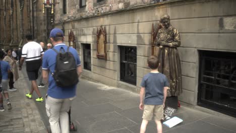 Fesselnde-Straßenszene-In-Edinburgh:-Ein-Mann-Macht-Ein-Foto-Einer-Interaktiven,-Mit-Kupfer-Bemalten-Marie-Curie-Statue,-Die-Durch-Spenden-Bewegt-Wurde