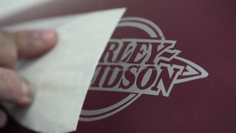 Worker-with-dirty-hands-removing-a-sticker-revealing-Harley-Davidson-logo-on-motorcycle-bodywork