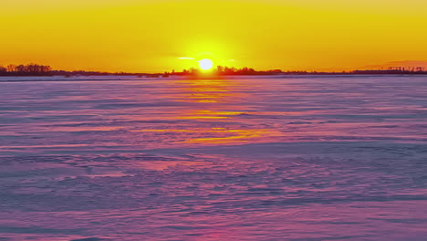 Sonnenaufgang-über-Einer-Gefrorenen-Ebene-Mit-Kaltem-Wind,-Der-über-Den-In-Gelbes-Und-Rosa-Licht-Getauchten-Schnee-Zieht