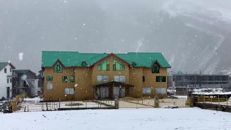 Zeitlupenszene-Mit-Schnee,-Der-Vor-Einem-Haus-In-Den-Ebenen-Von-Kaschmir-Fällt,-Umgeben-Von-Wohngebäuden-Und-Einem-Hohen-Schneeberg-Im-Hintergrund