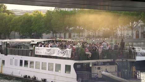 J'peux-Pas,-J'ai-Péniche-party-event-boat-passing-under-a-bridge-on-the-river-Seine,-Wide-shot