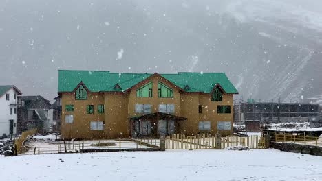 Front-View-of-slow-motion-scene-of-snow-falling-in-front-of-a-house-in-the-plains-of-Kashmir-surrounded-by-residential-buildings-and-a-tall-snow-mountain-in-the-background