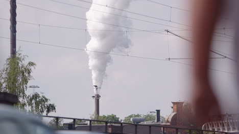 Plumes-of-smog-emissions-from-factory-smokestack,-street-view-of-people-passing