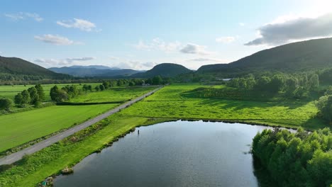 Aerial-Flyover-of-Fishing-Pond-in-the-Countryside-near-Small-Town-Ballater-in-Aberdeenshire,-Scotland-with-Forrest-Covered-Hills-on-a-Sunny-Summers-Day