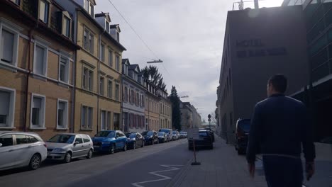 Man-walking-into-frame-near-cars-in-bavarian-downtown-near-road-in-Karlsruhe-Germany