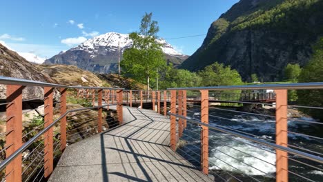 Walking-along-walkway-with-railings-beside-Geiranger-river-and-Norwegian-Fjord-center-in-Geiranger-Norway---Tourist-walking-point-of-view