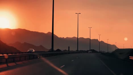 Brillo-Nocturno-De-La-Autopista-Qatar,-Omán,-Escena-Del-Amanecer-En-La-Autopista-Qatar-Express-Con-Silueta-De-Montaña,-Puesta-De-Sol-En-El-Fondo,-Hora-Dorada-Durante-La-Puesta-De-Sol-Tomada