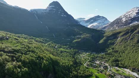 Impresionante-Geiranger-Noruega---Antena-De-Verano-Exuberante-Hacia-El-Mirador-Flydalsjuvet-Y-La-Carretera-Que-Va-Al-Cruce-De-La-Montaña---Unión-Hotelera-Apenas-Visible-En-El-Marco-Inferior-Y-El-Fiordo-Detrás-De-La-Cámara