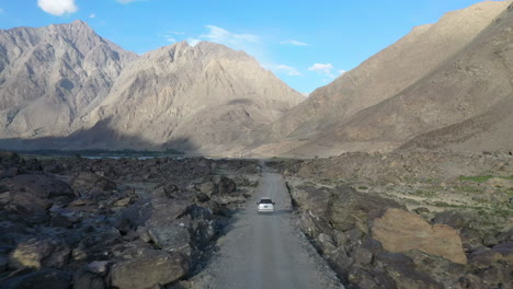 Drone-following-shot-of-a-vehicle-driving-on-a-dirt-road-in-the-Skardu-Valley-Pakistan,-with-the-mountain-range-in-the-distance