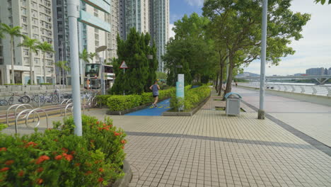 Mann-Läuft-In-Einem-Park-Mit-Skyline-Gebäuden-Im-Hintergrund-In-Einem-öffentlichen-Park,-Hongkong,-Kamerafahrt-Mit-Gimbal