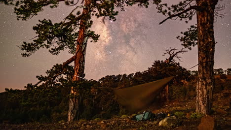 Timelapse-shot-of-star-movement-over-a-hiker-sleeping-in-a-hammock-swinging-between-trees-in-a-serene-camping-ground-along-Mount-Olympos,-Cyprus-at-night-time